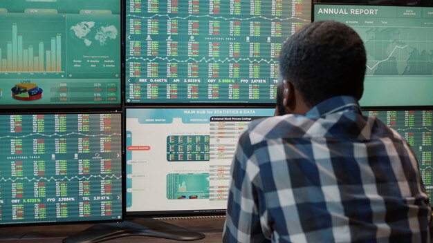 Afro-Amerikaanse man werkt met forex marktuitwisseling op multi-monitors werkstation, analyseert aandelenfondsen en kapitaalbankverkopen om winstgeld te kopen en verkopen. Financiële groei.
