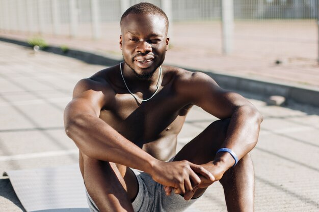 Afro-Amerikaanse man zit moe op de grond na het doen van zijn oefeningen