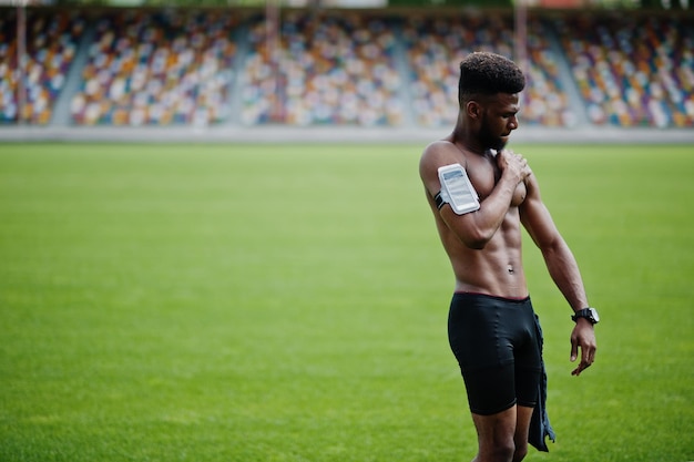 Afro-Amerikaanse mannelijke atleet sexy sport blote torso man met lopende sport arm case voor mobiele telefoon gesteld op groen gras van voetbalstadion