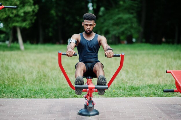 Afro-Amerikaanse mannelijke atleet sportman met lopende sportarmkoffer voor mobiele telefoon die oefeningen doet op straattrainingssimulators