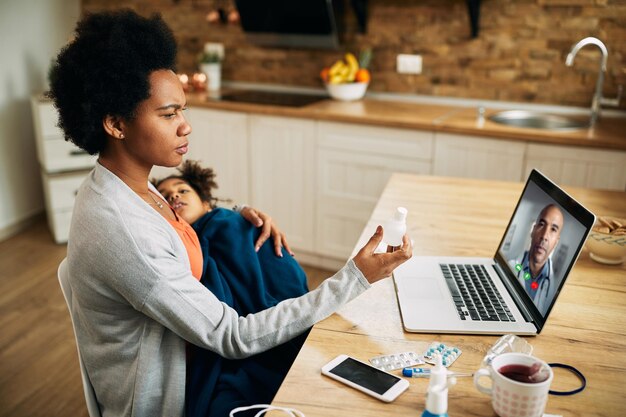 Afro-Amerikaanse moeder die videogesprek voert met een kinderarts terwijl ze een zieke dochter op schoot houdt