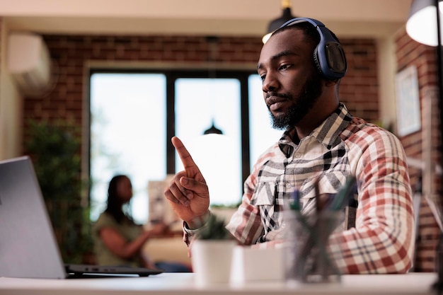 Afro-Amerikaanse student met draadloze koptelefoon in online videoconferentieles die omhoog wijst en handgebaar doet voor laptop. Mannelijke programmeur in internetoproep die wijsvinger opsteekt.