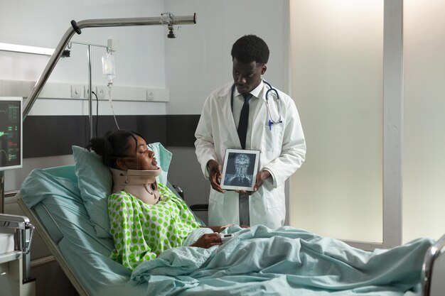 Afro-Amerikaanse therapeut arts die radiografie-expertise uitlegt aan zieke vrouw die de behandeling van de gezondheidszorg bespreekt tijdens een medische afspraak op de ziekenhuisafdeling. Patiënt met halskraag in de nek