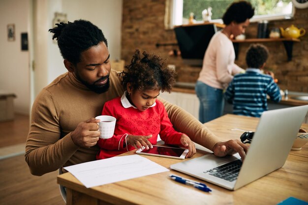 Afro-Amerikaanse vader en dochter die thuis draadloze technologie gebruiken