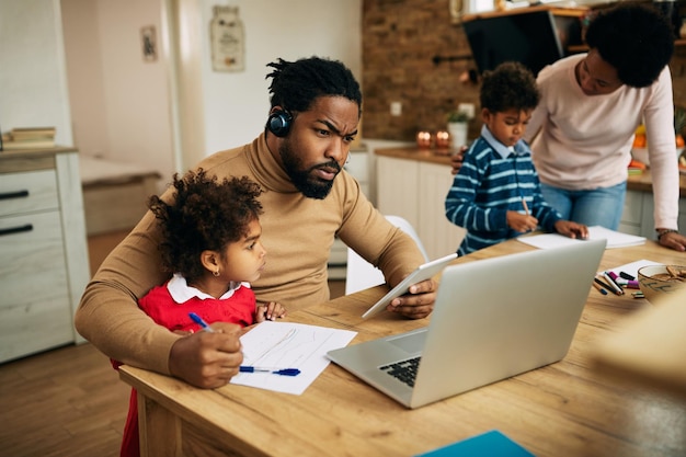 Afro-Amerikaanse vader multitasking terwijl hij thuis werkt