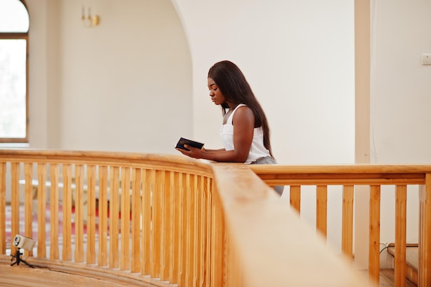 Afro-Amerikaanse vrouw die bidt in de kerk Gelovigen mediteert in de kathedraal en de spirituele tijd van gebed Afro-meisje met heilige bijbel bij de hand