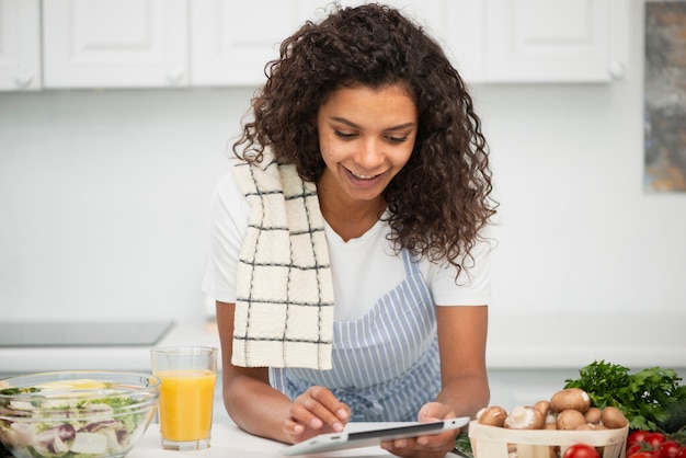 Afro Amerikaanse vrouw die op tablet in keuken kijkt