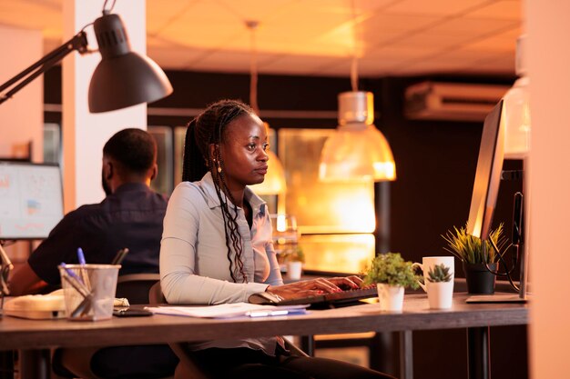 Afro-Amerikaanse vrouw die opstartproject op de computer doet, onderzoeksinformatie gebruikt om een bedrijfsrapport over e-mail te maken. Kijken naar online papierwerk op pc-monitor tijdens zonsondergang.