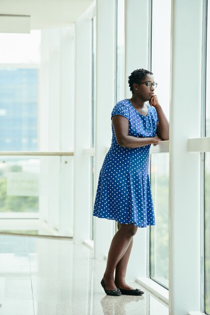 Afro-Amerikaanse vrouw die zich door venster in bureau bevindt en uit kijkt