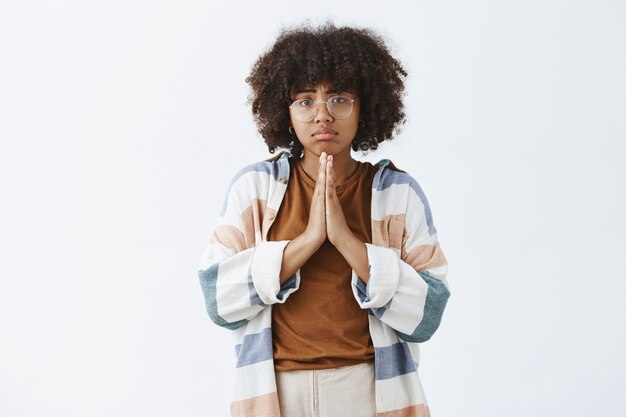 Afro-Amerikaanse vrouw in nood die somber en overstuur is, hand in hand in bid, fronsend en mokkend om gunst te vragen of om hulp te smeken