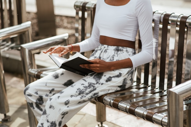 Gratis foto afro-amerikaanse vrouw zittend op een bankje en het lezen van een boek