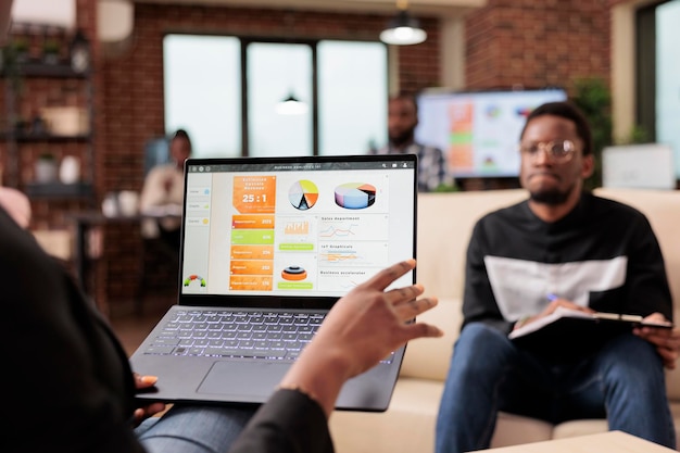 Afro-Amerikaanse zakenmensen die bedrijfsgrafieken en diagrammen op laptop analyseren om opstartpresentatie en papierwerkrapport te maken. Samenwerking in teamverband om onderzoeksinformatie te plannen.
