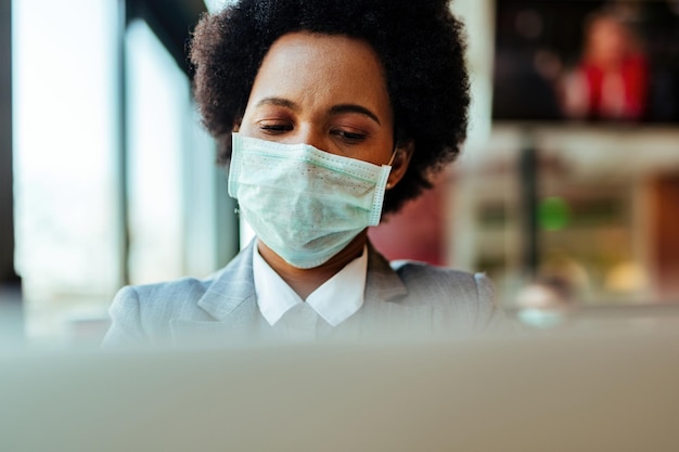 Afro-amerikaanse zakenvrouw die een beschermend masker op haar gezicht draagt terwijl ze aan een laptop werkt tijdens een virusepidemie