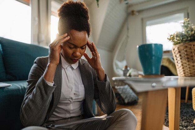 Afro-Amerikaanse zakenvrouw die hoofdpijn heeft en zich moe voelt terwijl ze thuis werkt