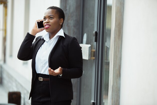 Afro-Amerikaanse zakenvrouw in kantoor kleding lachend, ziet er zelfverzekerd en gelukkig, druk