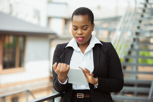 Afro-Amerikaanse zakenvrouw in kantoor kleding lachend, ziet er zelfverzekerd en gelukkig, druk