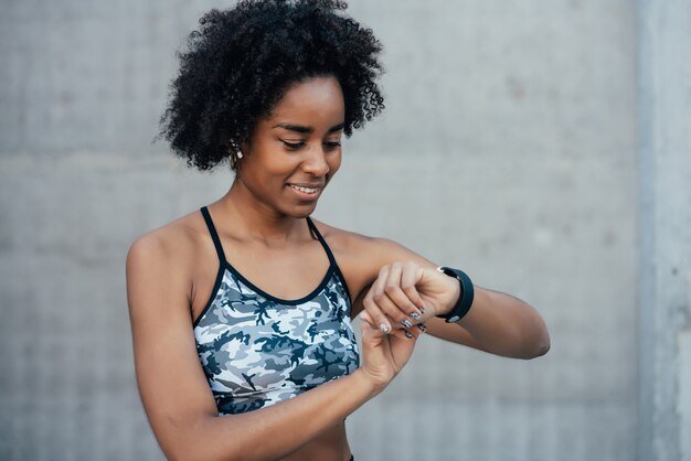 Afro-atletische vrouw die de tijd controleert op haar slimme horloge terwijl ze buiten aan het trainen is