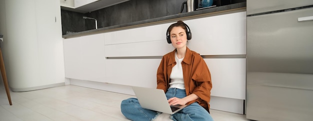 Afzonderlijke werkplek jonge vrouw werkt vanuit huis zit op de vloer met koptelefoon en laptop student doet