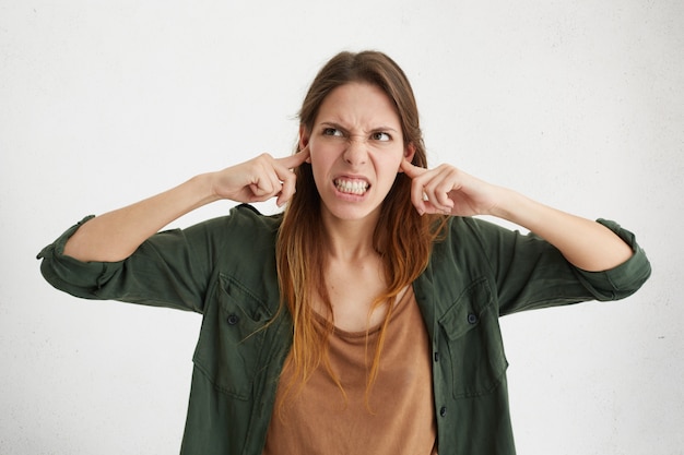 Agressief vrouwtje dat haar oren stopt die boos zijn op lawaai. Geïrriteerde jonge vrouw die harde geluiden probeert te vermijden