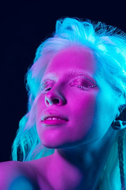 Albinomeisje met witte huid, natuurlijke lippen en wit haar in neonlicht dat op zwarte studioachtergrond wordt geïsoleerd.