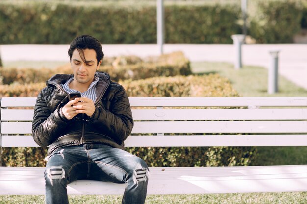 Alleenstaande man zittend op de bank in het park en praten met de telefoon. Hoge kwaliteit foto