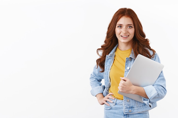 Gratis Foto ambitieuze schattige vrouwelijke student werkt freelance op afstand om collegegeld te betalen, laptop in de arm te houden, hand op taille te leggen professionele zelfverzekerde pose, glimlachend gemotiveerd, ga naar caféwerk