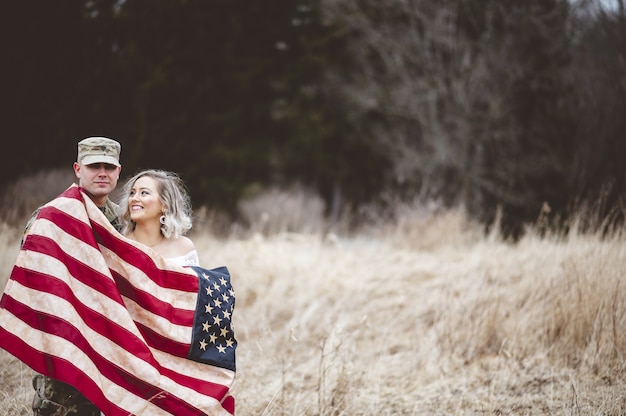 Gratis foto amerikaanse soldaat met zijn glimlachende vrouw gehuld in een amerikaanse vlag