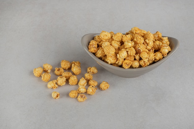 Amusekom gevuld met een portie popcorn met caramelcoating op marmer.