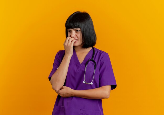 Angstige jonge brunette vrouwelijke arts in uniform met stethoscoop