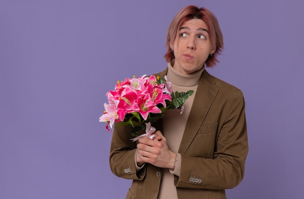 Angstige jonge knappe man die een boeket bloemen vasthoudt en naar de zijkant kijkt