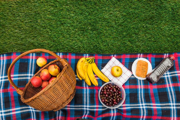 Appel; banaan; kersen; servet en bladerdeeg met waterfles op deken over groen gras