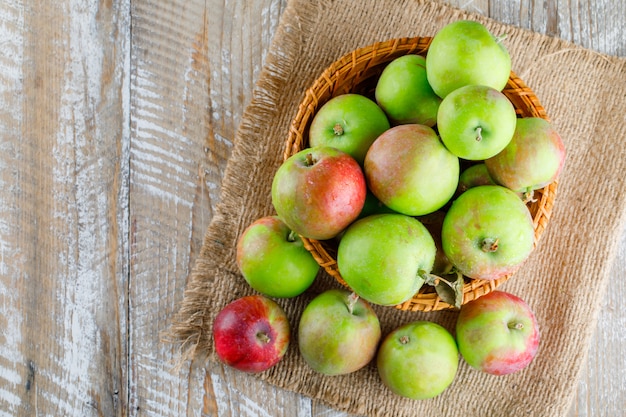 Appels in een rieten mand op houten en stuk zak.