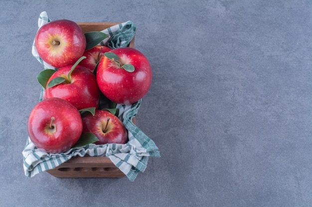 Appels met bladeren op handdoek op een doos op marmeren tafel.