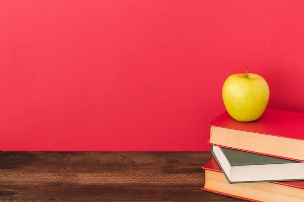 Gratis foto apple en boeken in de buurt van rode muur