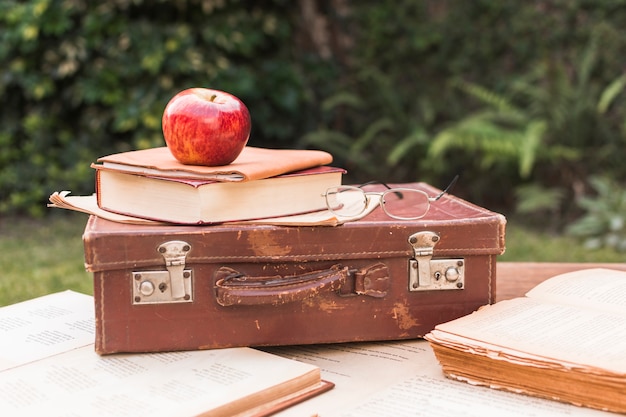 Gratis foto apple en glazen die op koffer dichtbij boeken liggen