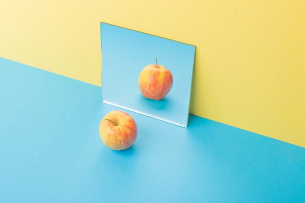 Apple op blauwe tafel geïsoleerd op geel in de buurt van spiegel