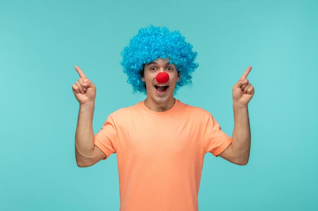 April dwazen dag kerel clown gelukkig wijzende vingers omhoog blauw haar opgewonden grappige rode neus