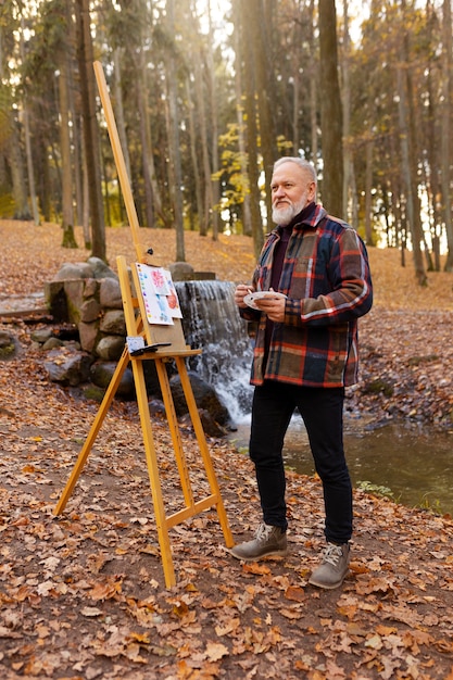 Gratis foto aquarelkunstenaar buiten in het bos met ezel en canvas