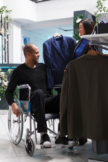 Gratis foto arabische man klant in rolstoel in gesprek met verkoper, bespreken jassen beschikbaar in kledingwinkel. klant met een handicap onderzoeken kleding stijl en grootte tijdens het winkelen voor formele outfit