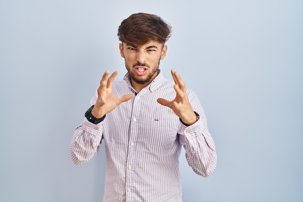 Gratis foto arabische man met baard die over blauwe achtergrond staat schreeuwend gefrustreerd van woede, handen proberen te wurgen, gek schreeuwend