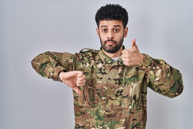 Arabische man met camouflage legeruniform doet duimen omhoog en omlaag, onenigheid en instemmingsuitdrukking. gek conflict