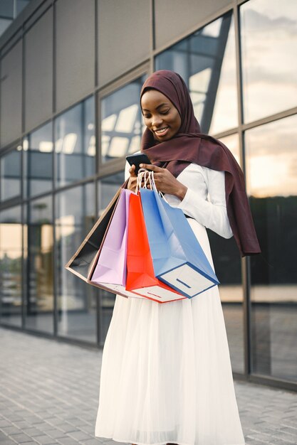 Arabische vrouw met hijab die met boodschappentassen staat en een telefoon gebruikt