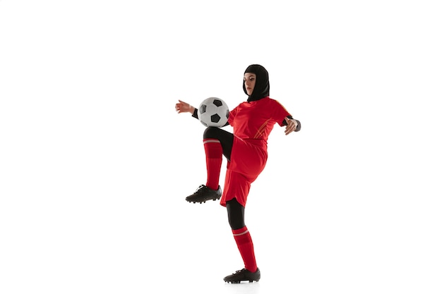 Arabische vrouwelijke voetbal of voetballer die op witte studioachtergrond wordt geïsoleerd. Jonge vrouw schoppen de bal, opleiding, oefenen in beweging en actie.
