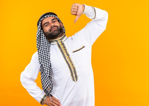 Arabische zakenman in traditionele kleding die naar zichzelf wijst zelfvoldaan gevoel trots staande over oranje muur