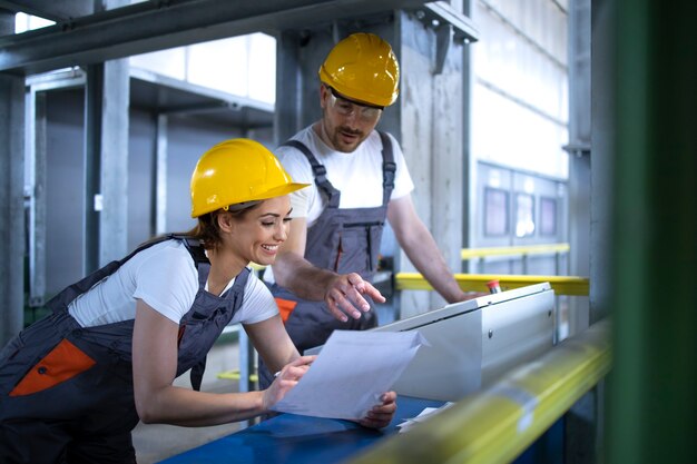 Arbeiders in uniformen en veiligheidshelmen die machines bedienen op de centrale fabriekscomputer