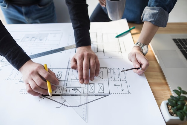 Architectenhanden die aan blauwdruk aan houten bureau op kantoor werken