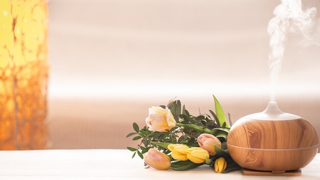 Aroma olie diffuser lamp op tafel op een onscherpe achtergrond met een prachtig lenteboeket tulpen.