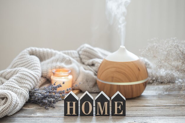 Aromastilleven met een moderne geuroliediffuser op een houten ondergrond met een gebreid element, knusse details en het decoratieve woord home.