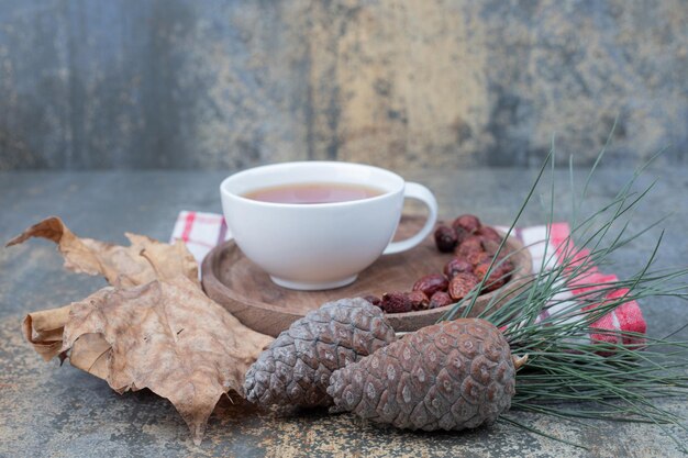 Aromathee in witte kop met rozenbottels en dennenappels op marmeren tafel