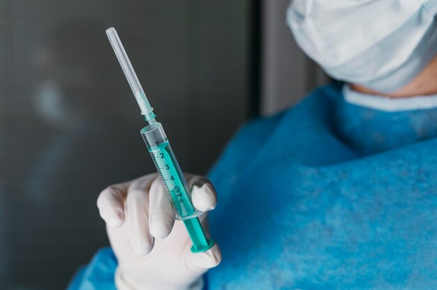 Arts die een vaccinfles vasthoudt terwijl hij beschermende uitrusting draagt